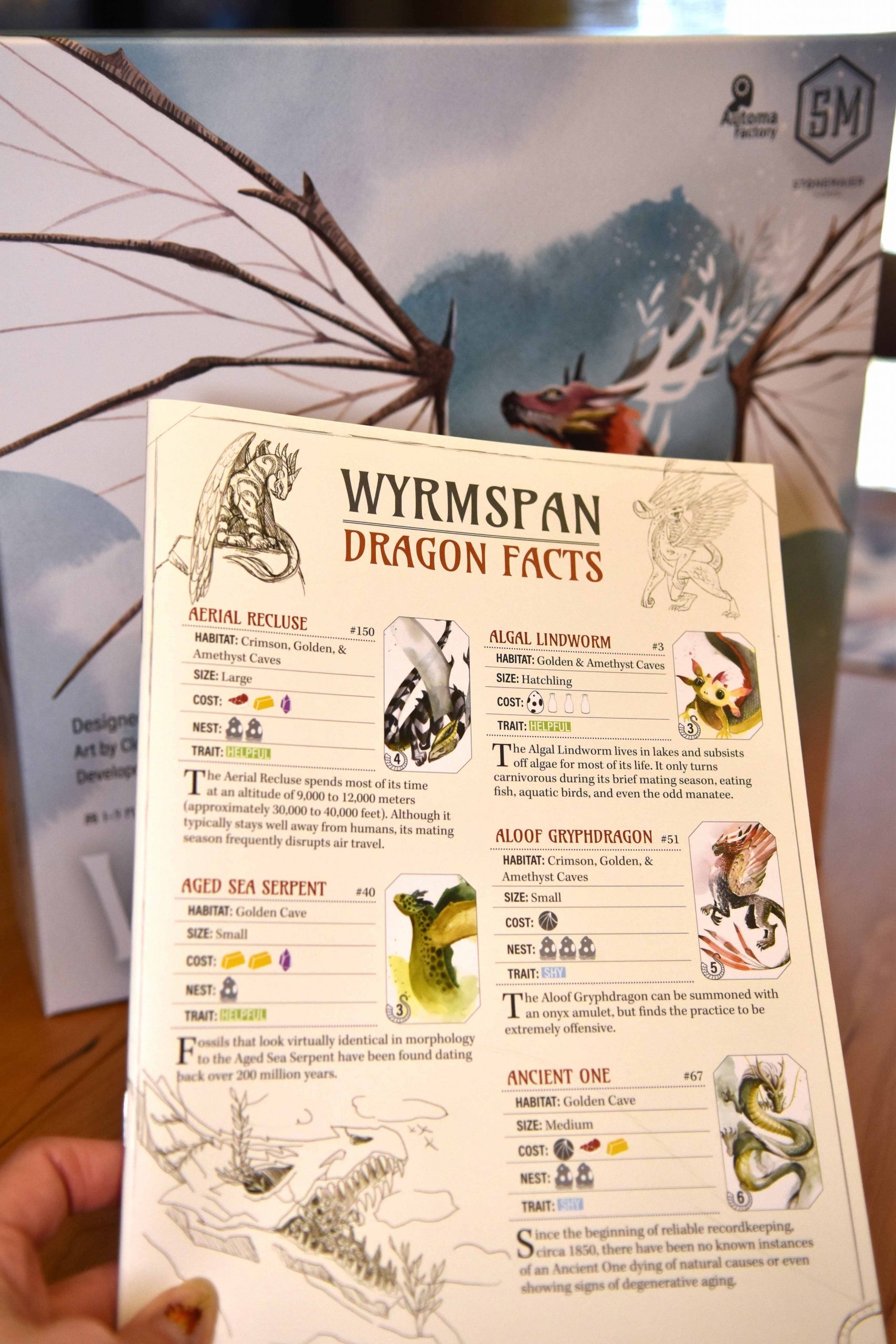 Wyrmspan dragon almanac open beside cards