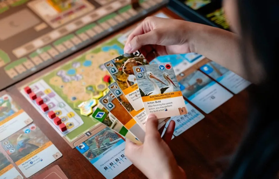 Ark Nova animal cards held in front of a player zoo map