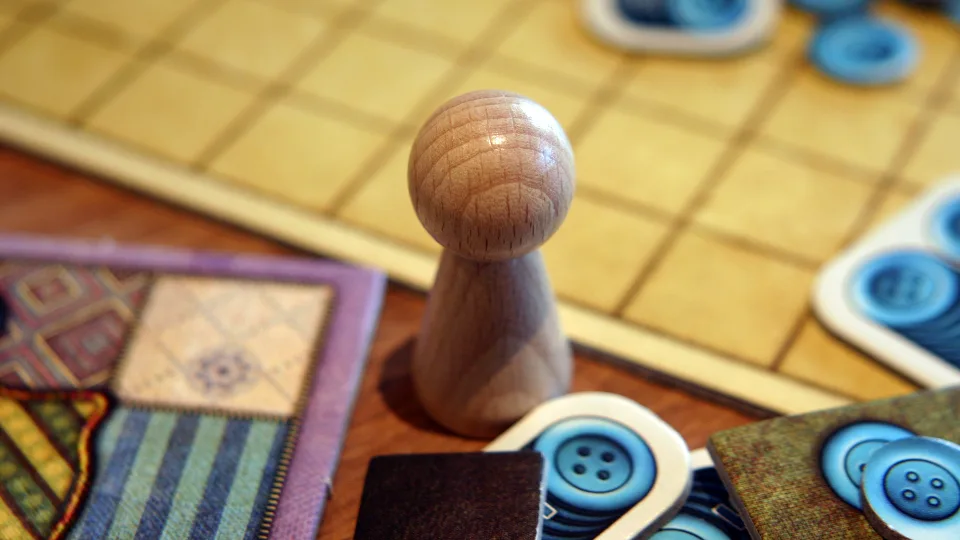 Patchwork wooden time marker beside quilt board and button tokens.