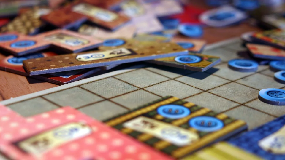 Patchwork quilt boards, patch tiles, buttons, and wooden player markers arranged on a table.